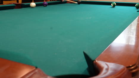 Man-Playing-8-Ball-Pool-Scratches-Cue-Ball-in-the-Side-Pocket-on-a-Brunswick-Table-with-Green-Felt-and-Several-Balls-Left-on-the-Table,-Open-Bridge-Hand-and-Wooden-Cue-Stick,-Low-Angle-no-faces