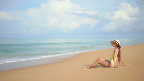A-pretty-young-fit-woman-sits-on-a-sandy-beach-in-Southeast-Asia-enjoying-the-sun-while-the-waves-roll-in
