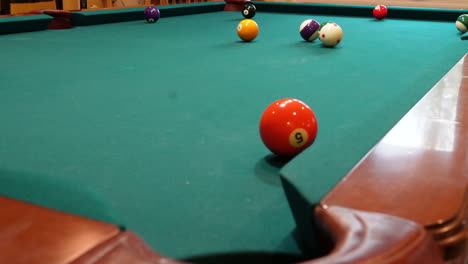 8-Ball-Pool-Table-Where-Orange-Striped-13-Ball-is-Shot-into-the-Corner-Pocket-Closeup-With-Several-Balls-Left-on-a-Brunswick-with-Green-Felt-or-Cloth-using-Follow-Spin-on-the-Cue-Ball,-Low-Angle