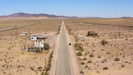 Old-route-66-stretching-down-the-desert-in-a-straight-line-passing-by-a-burnt-down-gas-station-and-old-houses
