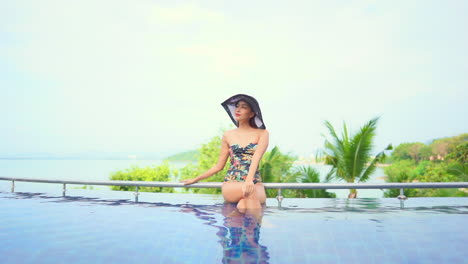 Asian-woman-in-swimsuit-sitting-on-pool-edge-and-looking-around-with-satisfaction