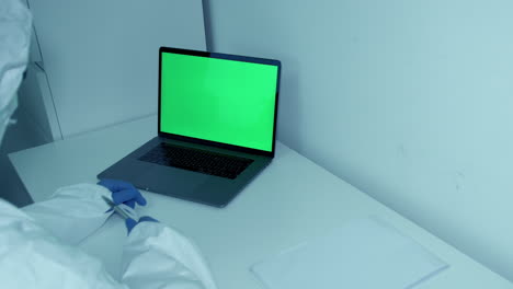 Hospital-worker-in-protective-scrubs-gestures-and-points-to-green-screen-laptop-notes