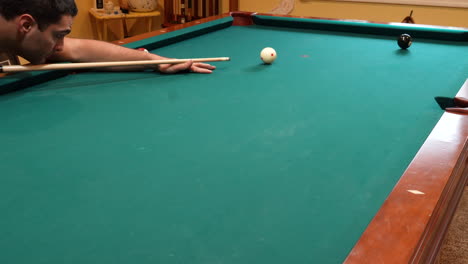 Man-Playing-8-Ball-Pool-Shoots-Solid-Black-Eight-Ball-into-Corner-Pocket-to-Win-the-Game-on-a-Brunswick-Table-with-Green-Felt-in-Basement-of-Home,-Open-Bridge-Hand-and-Wooden-Cue-Stick,-Wide-Angle