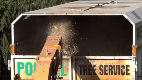 Medium-shot-of-wood-chips-expelled-from-chute-of-wood-chipper-into-the-back-of-a-truck-in-slow-motion