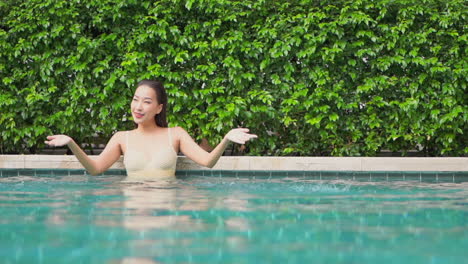 An-excited-Asian-woman-in-a-swimming-pool-splashing-water-with-her-hands,-slow-motion