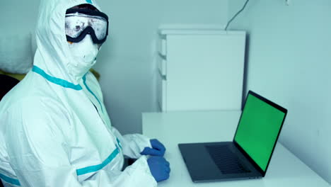Doctor-healthcare-worker-looking-from-computer-green-screen-to-camera-in-protective-mask-gear