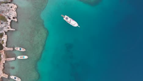 Boat-Floating-On-Turquoise-Blue-Sea-Near-The-Shore-In-Phaselis,-Antalya,-Turkey---aerial-orbiting-drone