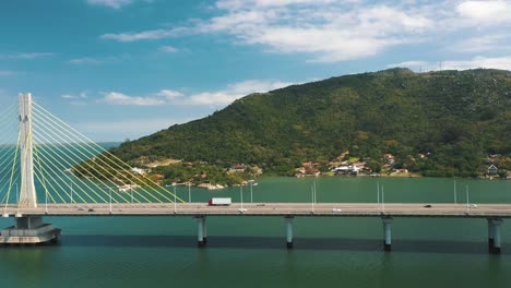 Konkrete-Schrägseilbrücke-Verkehr-über-Türkisfarbenem-Ozean-Drohne-Luftseitenschwenk-Blick-Auf
