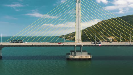Drone-aerial-side-panning-view-of-concrete-cable-stayed-bridge-traffic-above-turquoise-color-ocean