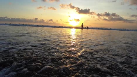 Waves-flowing-ashore-on-the-beach-in-a-sunset-at-Bali,-Indonesia-while-the-sun-is-setting-golden-beautiful