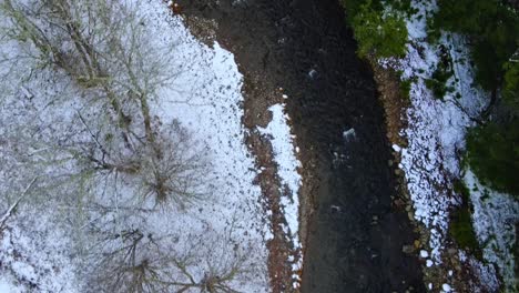 Aerial-footage-of-a-mountain-stream-in-the-winter-with-fresh-snowfall