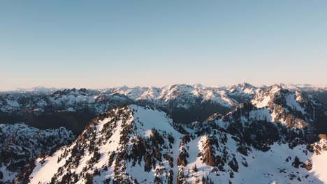 A-high-orbiting-drone-shot-of-a-snowy-peak-in-the-Olympic-mountains-taken-from-just-outside-the-national-park-at-sunset