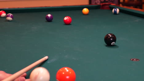 Person-Playing-Pool-Shoots-Green-Striped-14-Ball-into-Far-Corner-Pocket-using-Draw-or-Backspin-on-the-Cue-Ball,-closeup-of-Bridge-Hand-with-Wooden-Cue-Stick-Digging-Into-Green-Felt-or-Cloth