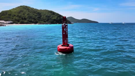 Aerial-4k-drone-footage-circling-a-red-buoy-bobbling-in-the-waves-near-the-coastline-of-the-exotic-resort-of-Ko-Larn,-Thailand