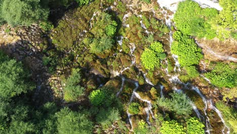 Mountainside-waterfall-cascading-over-rocks,-aerial-top-down-view
