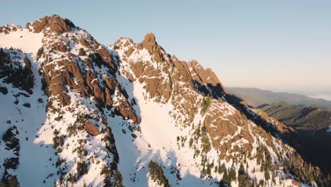 Eine-Aufsteigende-Und-Nach-Unten-Schauende-Drohnenaufnahme-Eines-Schneebedeckten-Gipfels-In-Den-Olympischen-Bergen,-Aufgenommen-Direkt-Außerhalb-Des-Nationalparks-Bei-Sonnenuntergang