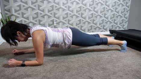 Hispanic-female-holding-a-plank-position-in-home-gym,-exercising