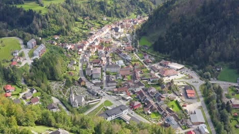 Drone-shot-of-a-town-surrounded-by-the-lush-green-mountain-landscape-at-Eisenkappel-Vellach,-Austria