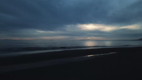 Dark-view-of-empty-beach-with-calm-waves-and-dramatic-sky