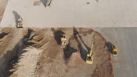 Birds-eye-drone-view-of-construction-vehicles-moving-dirt-around-a-concrete-pad-at-a-busy-construction-site-during-a-cloudy-winter-day