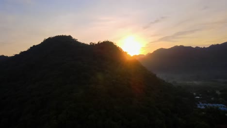 4k-drone-footage-revealing-a-beautiful-sunset-over-a-vast-valley-from-behind-a-mountain-in-Khao-Yai,-Thailand