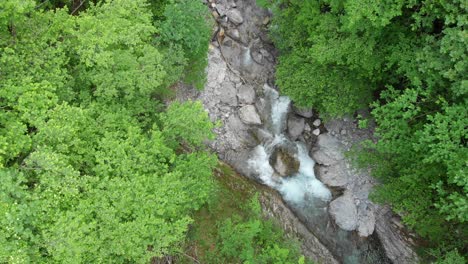 drone-lifts-above-small-stream-in-forest,-top-down-river-view,-slovenia