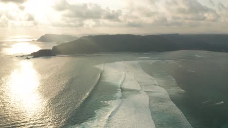 Tranquil-lines-of-waves-roll-into-Laut-Lombok-bay-during-sunset,-aerial