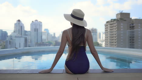 Woman-sitting-on-pools-edge-looking-over-city-sky-line