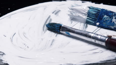 Three-wet-paintbrushes-jostled-on-white-paint-swirl