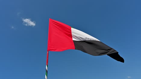 4k-Aufnahmen:-Nationalflagge-Der-Vereinigten-Arabischen-Emirate-Auf-Einer-Stange,-Die-Im-Wind-Gegen-Den-Klaren-Blauen-Himmel-Weht,-Ein-Teil-Der-Feierlichkeiten-Zum-Nationalfeiertag-Der-Vereinigten-Arabischen-Emirate