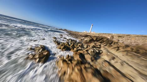 Amazing-drone-FPV-low-over-ocean-waves-rocks-to-passing-lighthouse-on-coastline