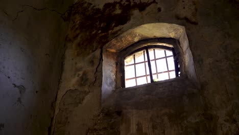 Window-of-dungeon-with-irons-and-ruined-dirty-walls-inside-medieval-fortress,-historic-place
