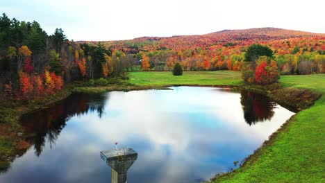 Lebendige-Herbstlandschaft,-Blaues-Teichwasser-Mit-Himmelsspiegelreflexion-Und-Buntem-Waldlaub,-Drohnenluftbild