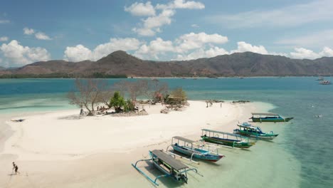 Flying-over-tiny-island-Gili-Kedis-with-local-boats-on-shore-for-tourist,-aerial