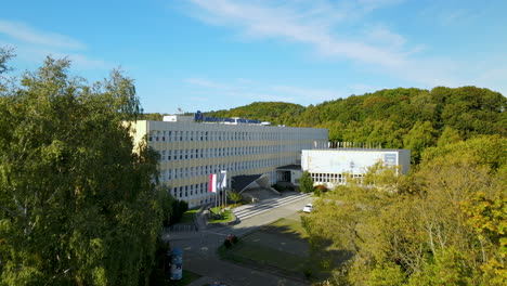 Aerial-dolly-forward-drone-shot-of-modern-university-building-facade-with-sunny-trees