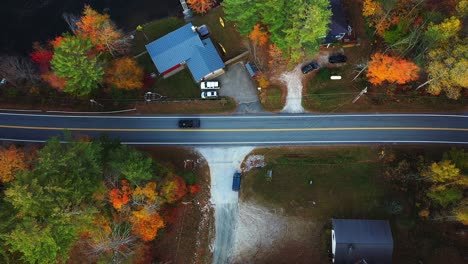 Birds-Eye-Aerial-View-of-Cars-on-Countryside-Road-by-Houses-and-Colorful-Forest-on-Autumn-Day,-Top-Down-Descending-Drone-Shot
