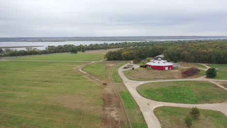 Aerial-view-of-a-grassy-farm-yard-in-Illinois-with-a-red-barn-and-the-river-in-the-background
