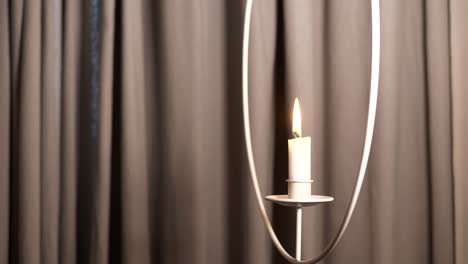 Beautiful-shot-of-burning-hanging-candle-against-plain-coloured-background-curtain