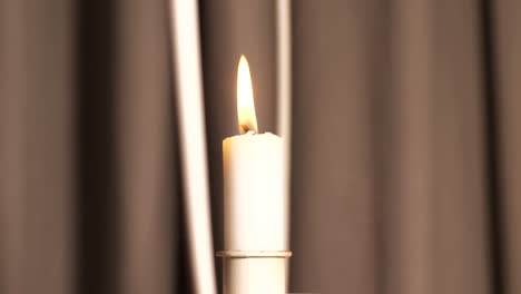 Close-up-of-smoke-rising-by-moving-candle-with-curtains-in-background