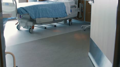 Tilt-up-through-a-doorway-into-an-empty-hospital-room,-revealing-an-empty-hospital-bed