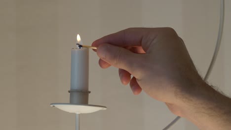 Male-hand-lights-candle-on-hanging-holder-with-match,-slomo-close-up