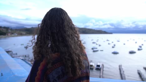 Girl-Looks-Over-Boats-in-Lake-Titicaca,-View-from-Behind-with-Hair-Blowing-in-Wind