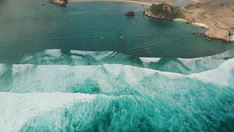Whitewater-waves-roll-over-shallow-reef-towards-shore-of-Lombok,-aerial