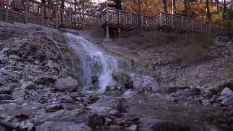 Heißes-Wasser,-Das-Den-Wasserfall-Neben-Den-Felsen-Im-Park-Mit-Holzplattform-Herunterläuft