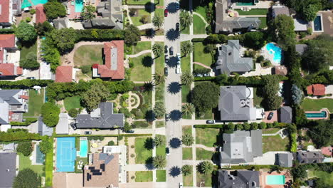 Drone-shot-flying-over-beauitufl-palm-tree-lined-streets-with-silver,-white-and-black-cars-driving,-the-streets-surrounded-by-mansions-with-swimming-pools-in-West-Hollywood,-Los-Angeles,-California