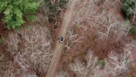 An-aerial-of-a-vehicle-on-a-dirt-road-in-the-forest-during-the-winter-season