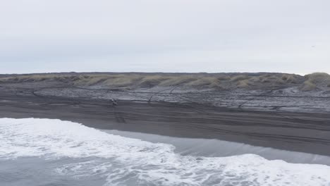 Quad-bike-pulling-a-wheelie-on-black-sand-beach-in-Iceland,-aerial