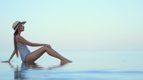 An-elegant-woman-enjoys-warm-sea-on-the-tropical-coast,-FItt-model-sitting-in-shallow-sea-water,-side-view,-slow-motion