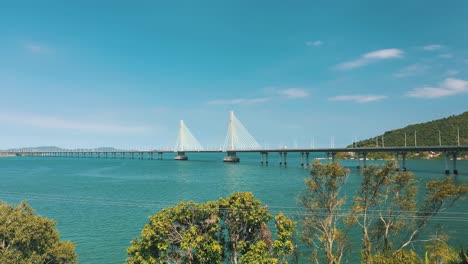 Drone-aerial-side-view-of-concrete-cable-stayed-bridge-road-above-turquoise-color-tropical-ocean,-located-in-Laguna,-Santa-Catarina,-Brazil