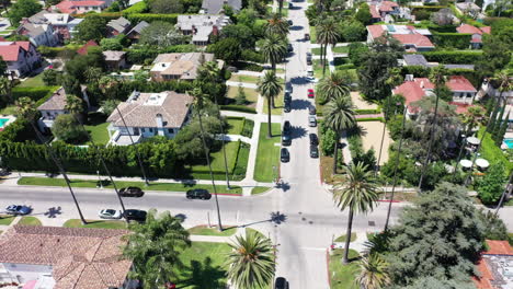 Drone-zooms-out-to-reveal-palm-tree-lined-streets-with-cars-driving,-and-mansions-in-West-Hollywood,-California